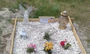 Grzebowisko dla zwierząt z aniołem, lampionem, wazonem i tabliczką z napisem "ROLEX" oraz zdjęciem psa.